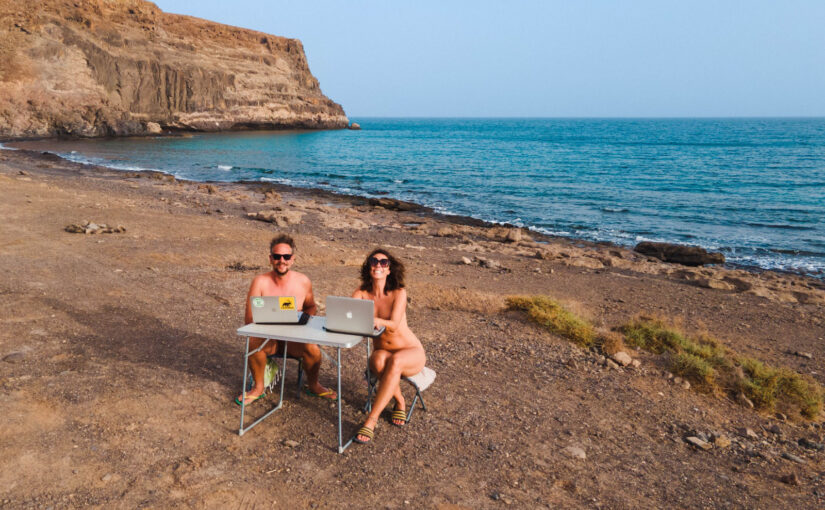 Nick and Lins of Naked Wanderings on a beach with their computers